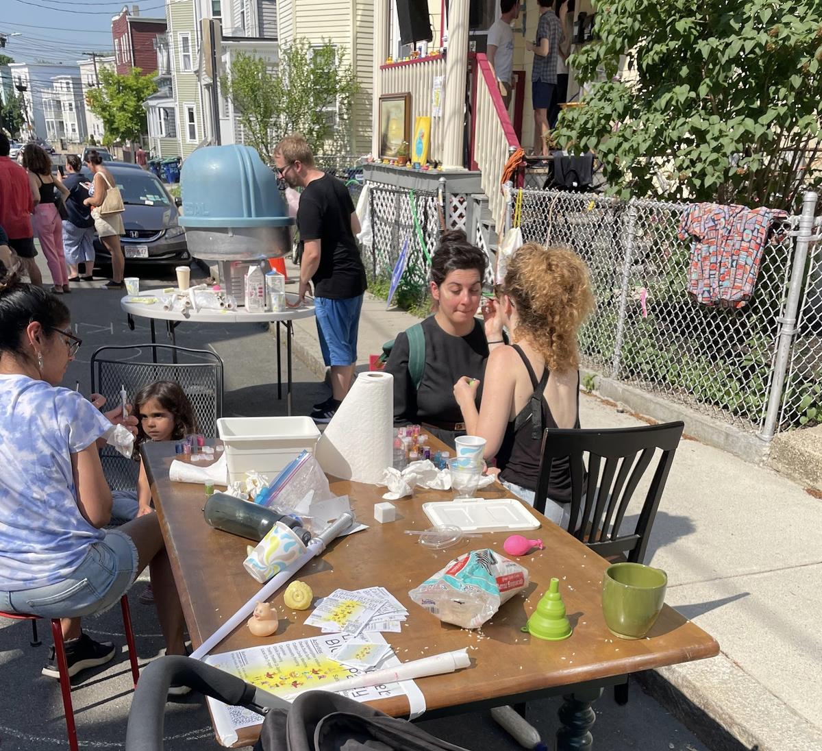 A photo of people face painting sitting at a table on the street during a Block Party