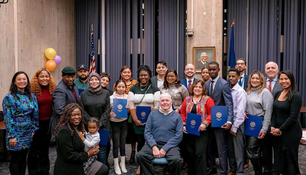 Twenty participants of Immigrants Lead Boston 2022 pose with blue graduation certificates